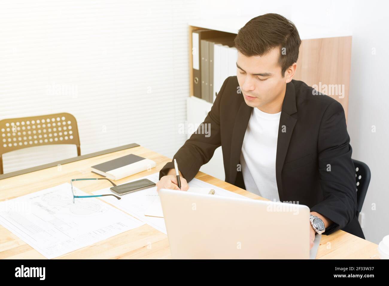 Geschäftsmann schreiben, während mit Laptop-Computer im Büro Stockfoto