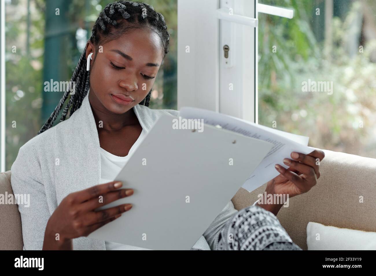 Nachdenklich hübsche junge Frau, die von zu Hause aus arbeitet und Vertrag liest Oder Finanzdokument beim Sitzen auf dem Sofa Stockfoto