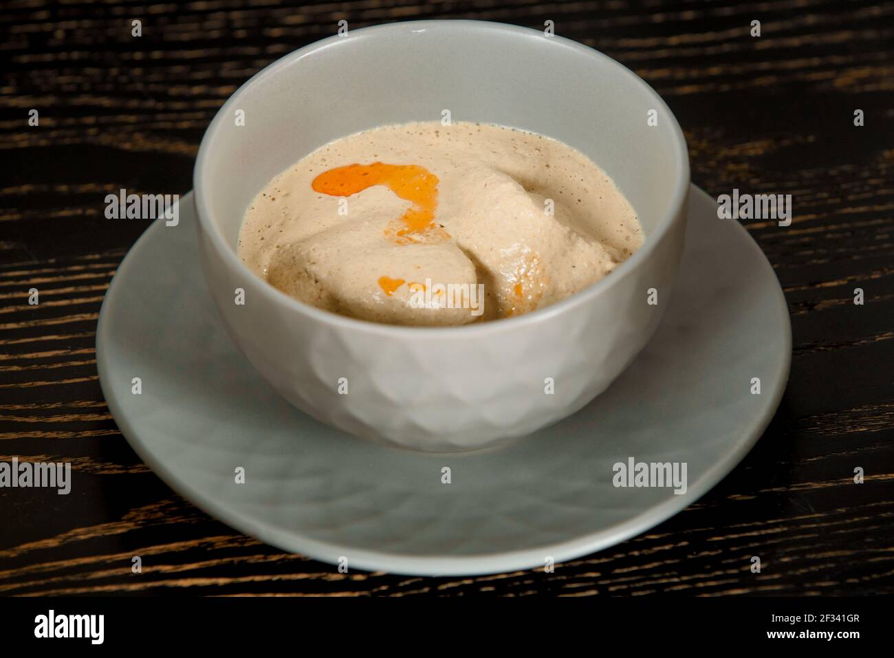 Cremige dicke Suppe mit Fleisch in einer grauen Schüssel auf einem dunklen Holztisch. Stockfoto