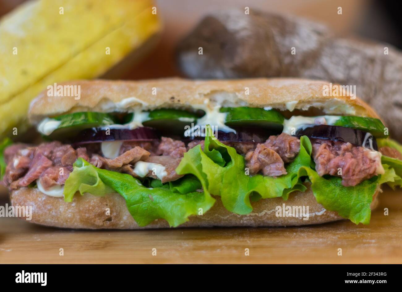 Thunfisch-Sandwich mit roten Zwiebeln, Salladen und Gurkenscheiben, die sich auf einem Holztisch bewegen Stockfoto