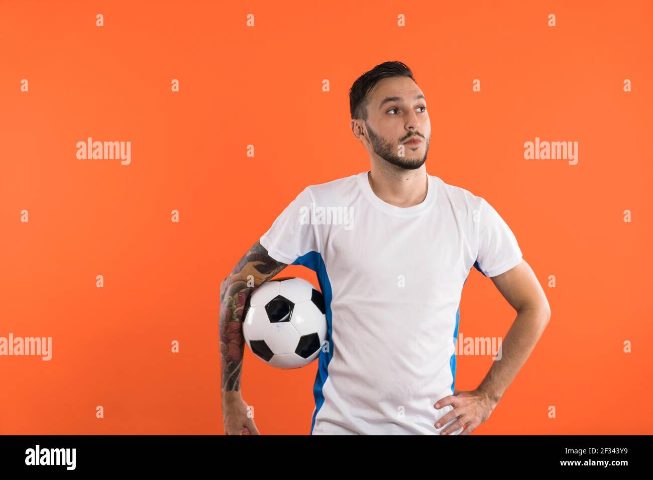 Fußballspieler hält einen Ball isoliert auf orangefarbenem Hintergrund Stockfoto