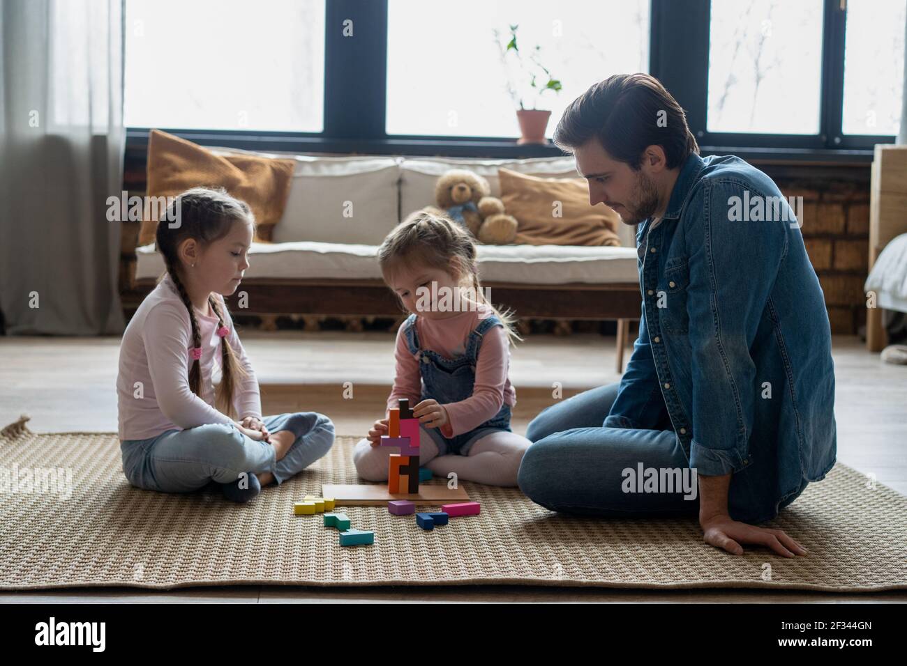 Liebevoller junger Vater liegt auf dem Boden mit kleinen Kindern haben Spaß in lustige Aktivität mit Bausteinen beschäftigt Stockfoto