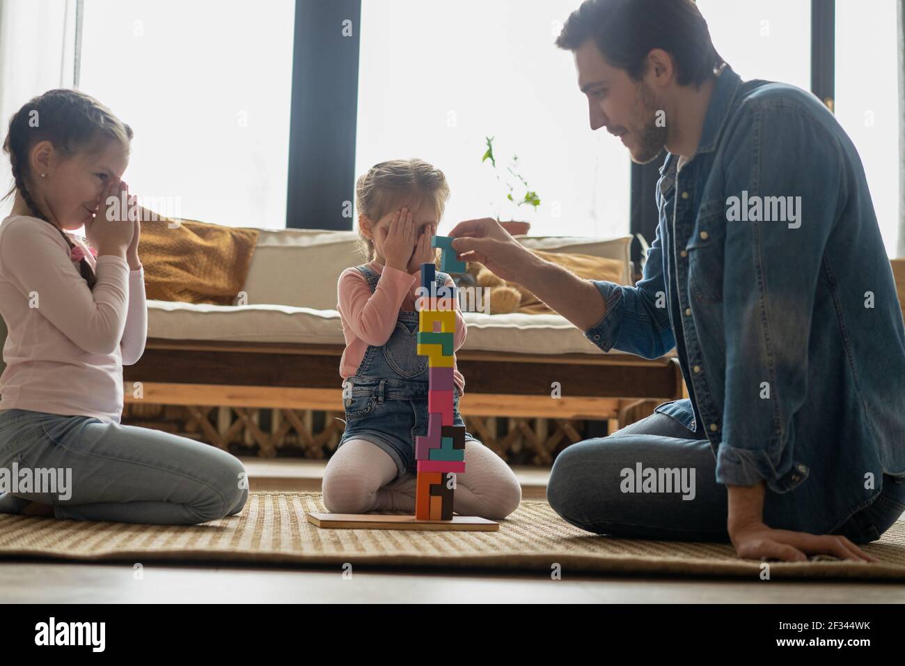 Liebevoller junger Vater liegt auf dem Boden mit kleinen Kindern haben Spaß in lustige Aktivität mit Bausteinen beschäftigt Stockfoto
