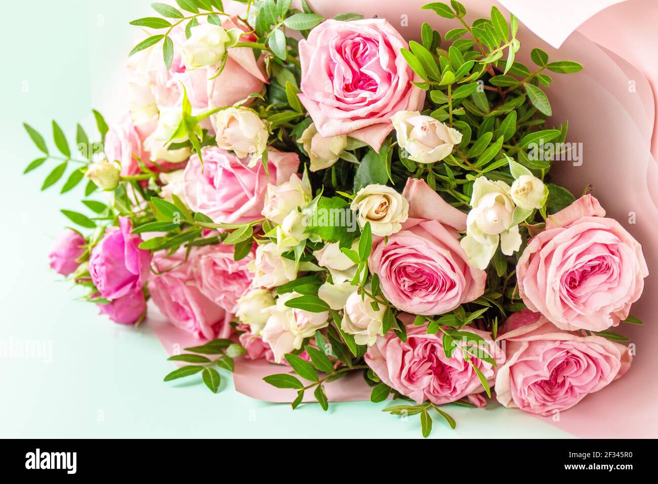 Muttertag, Frauentag oder Geburtstagsgrüße Konzept. Schönes Bouquet von blühenden zarten rosa Rosen und Frühlingsgrün auf grünem Hintergrund. Stockfoto