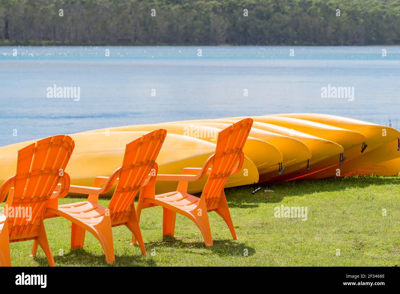 Orangefarbene Stühle und gelbe Kanus am Lake Conjola an der Südküste von New South Wales verbinden sich mit grünem Gras und blauem Wasser. Stockfoto
