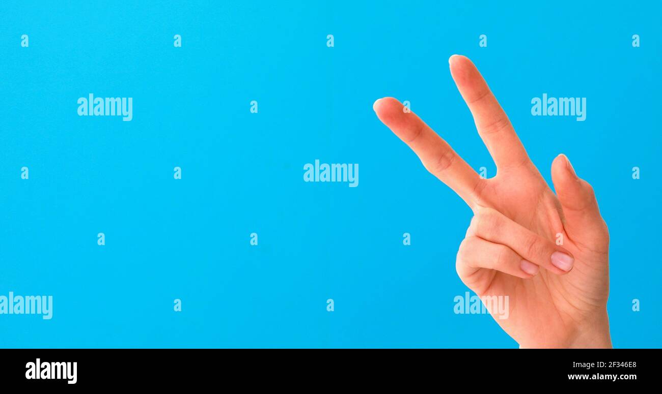Nahaufnahme der schönen weiblichen Hand tun Siegeszeichen, isoliert auf blauem Studio-Hintergrund mit Kopieplatz für Gegner. Konzept der Körpersprache. Hand Stockfoto