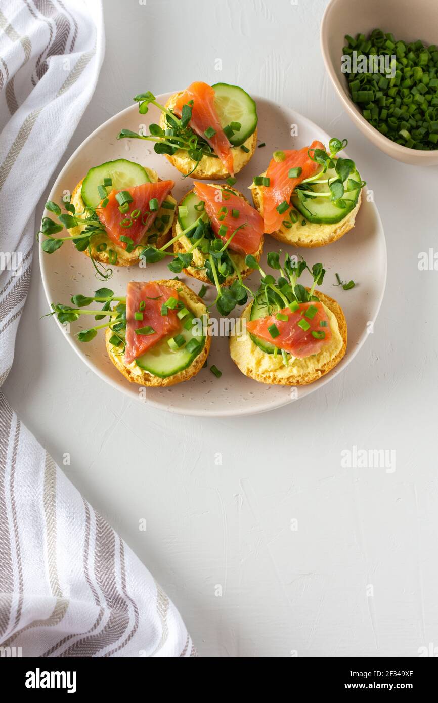 Leckere herzhafte Vorspeise, Lachsbraten auf einem weißen Teller, rundes gebratenes Brötchen mit rotem Fisch, Gurke, Sauce Hollandaise und Erbsensprossen Stockfoto