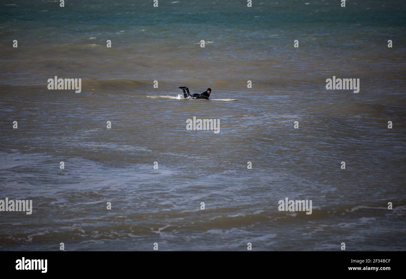 Ein lokaler Surfer am Strand von West Wittering hält sich in sozialer Distanz, da der Parkplatz geschlossen werden muss, nachdem am Samstag Tausende von Menschen auftauchten. Stockfoto