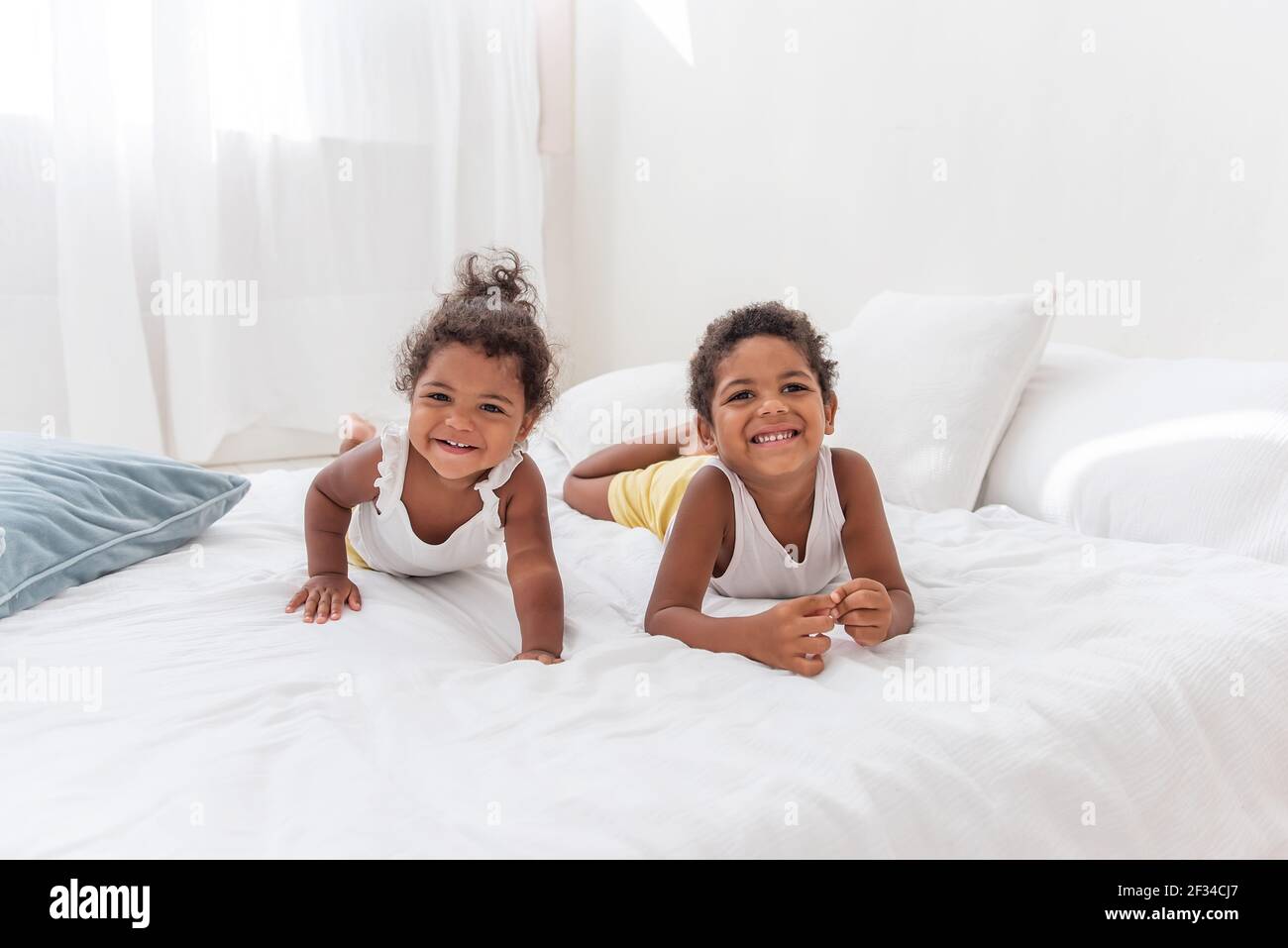 Bruder und Schwester Afroamerikaner spielen zusammen auf weißem Bett in einem Loft-Innenraum. Geschwister haben Spaß unter den blauen Kissen am Morgen. Schließen-U Stockfoto