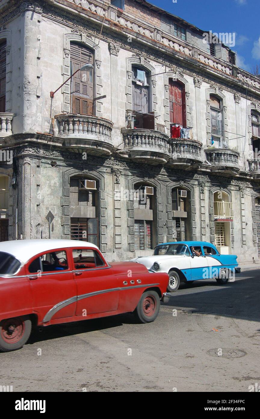Zwei Oldtimer, die an einem sonnigen Tag als Sammeltaxi-Taxis benutzt werden, die entlang einer Straße in Zentral-Havanna, Kuba, fahren. Stockfoto