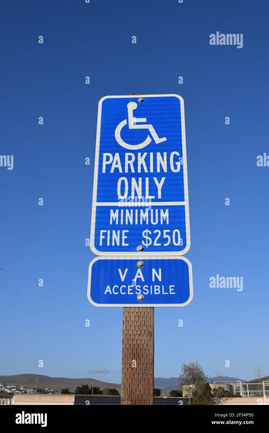 Eine vertikale Aufnahme eines blauen Schildes mit der Aufschrift ''Parking only, Minimum Fine $250, Van accessible'' am Strand Stockfoto