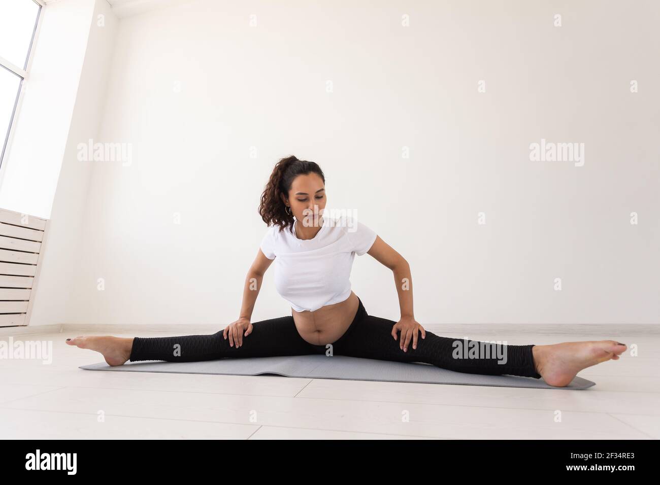 Zielgerichtete schwangere Frau übt während des Yoga-Kurses und entspannt sich, während sie auf einer Matte auf dem Boden sitzt. Konzept der körperlichen und geistigen Vorbereitung von Stockfoto