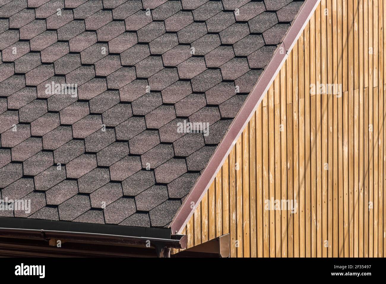 Modernes Gebäudeelement mit gefliestem dunklen Dach und Holzwandhintergrund. Stockfoto