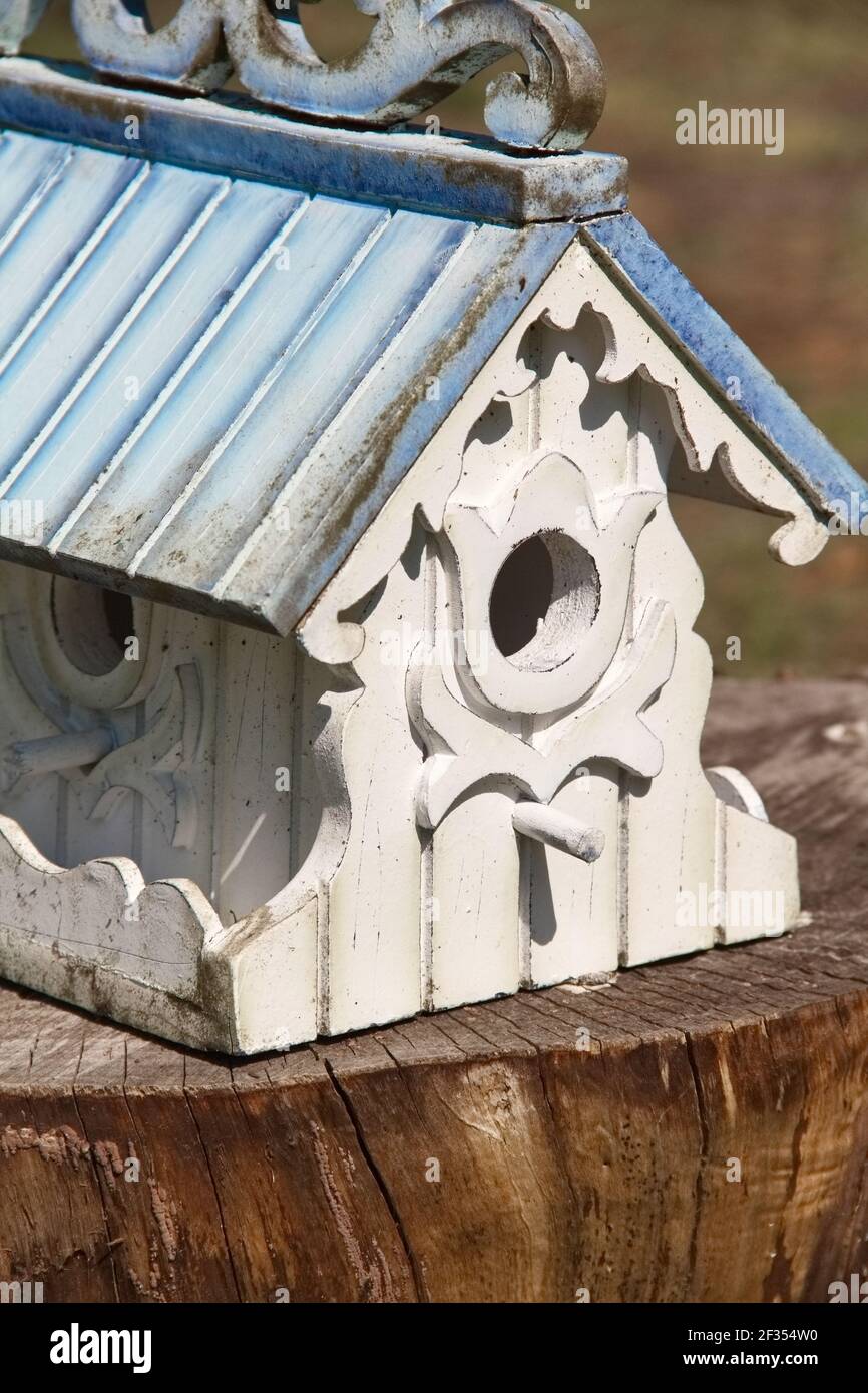 Aufwendig gebaute weiße Vogelhaus mit hellblauem Dach und gedeckelt Verzierte Besatz zeigt zwei Öffnungen mit Sitzstangen auf einem Brauner Baumstumpf Stockfoto