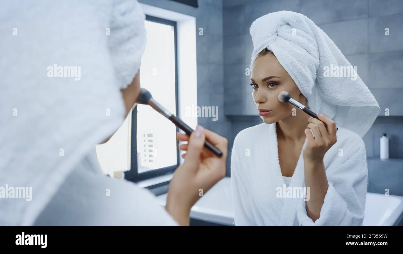 Junge Frau, die Gesicht Pulver mit kosmetischen Pinsel beim Suchen Am Spiegel im Badezimmer Stockfoto