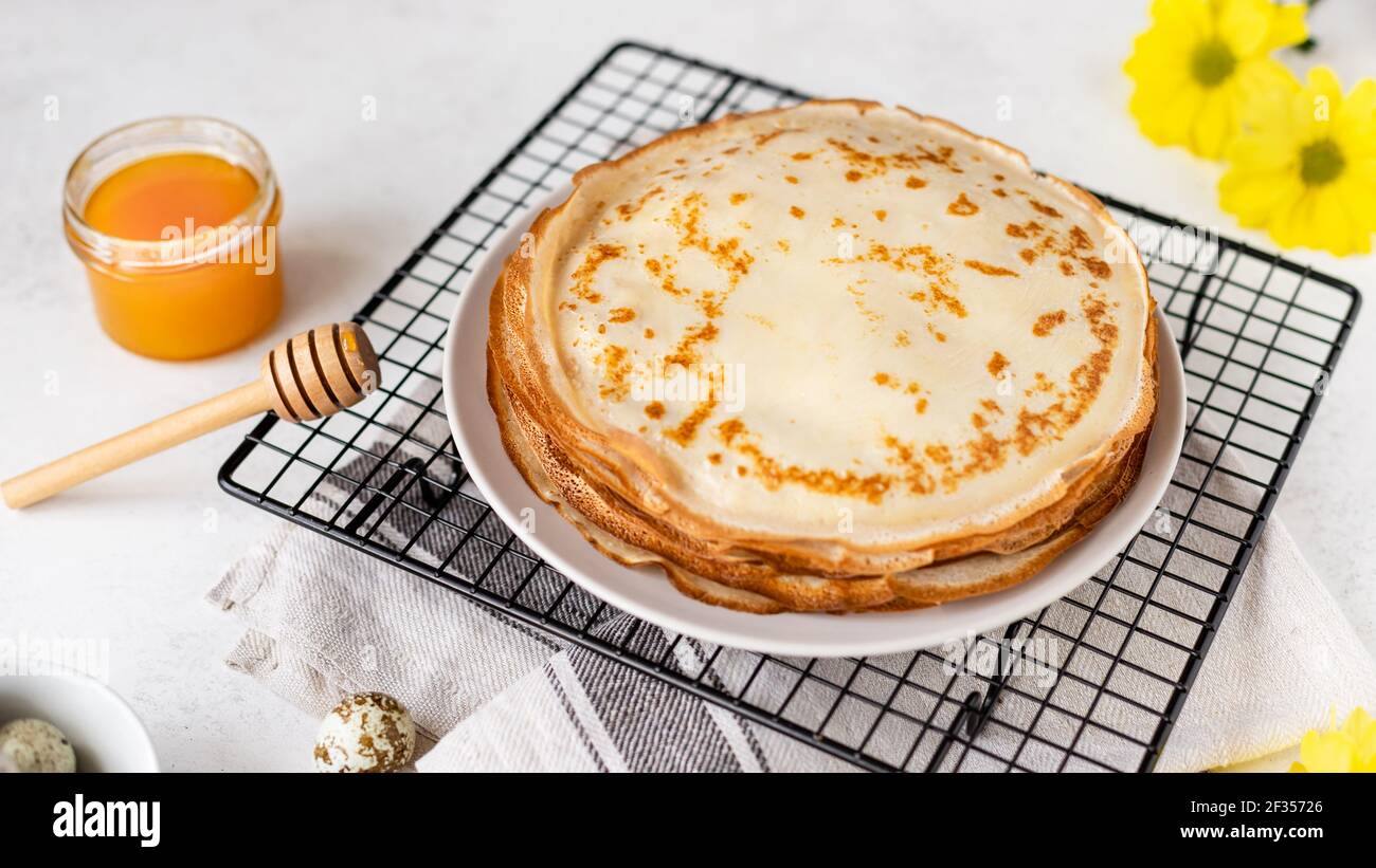 Traditionelle hausgemachte dünne Pfannkuchen, Blini mit Honig auf weißem Hintergrund mit Frühlingsblumen. Russische Maslenitsa. Horizontales Bild, Seitenansicht Stockfoto