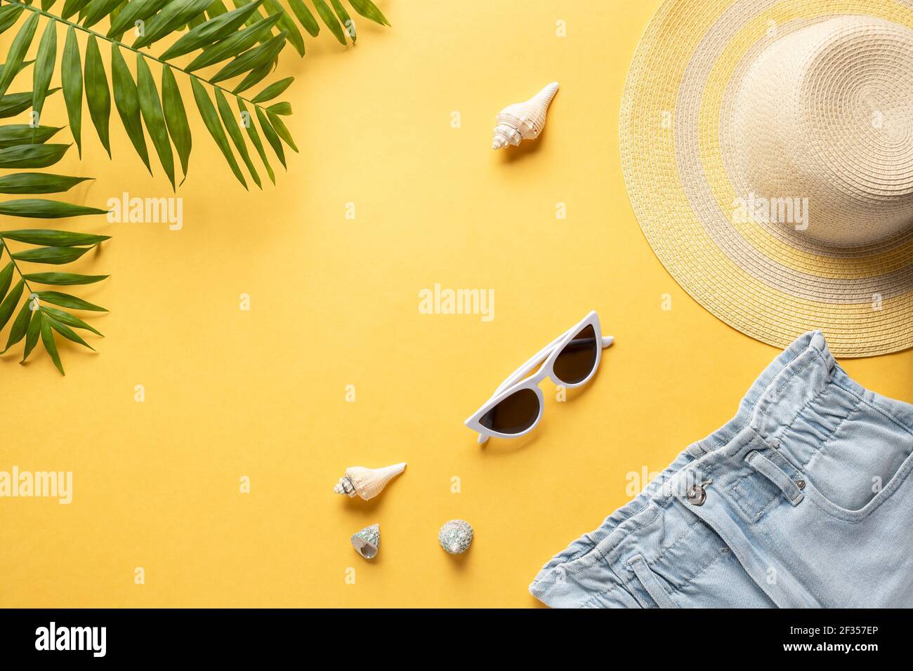 Strohhut, Sonnenbrille, blaue Denim-Shorts und Palmenblätter auf gelbem Hintergrund. Konzept Sommerurlaub Hintergrund. Horizontales Bild. Copy space Stockfoto