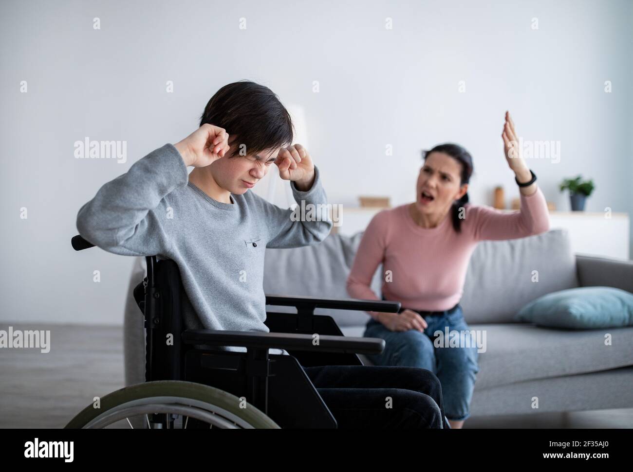 Teenager Junge im Rollstuhl kämpfen mit seiner verärgerten Mutter, Ohren schließen, nicht zu hören, wie sie zu Hause streiten Stockfoto
