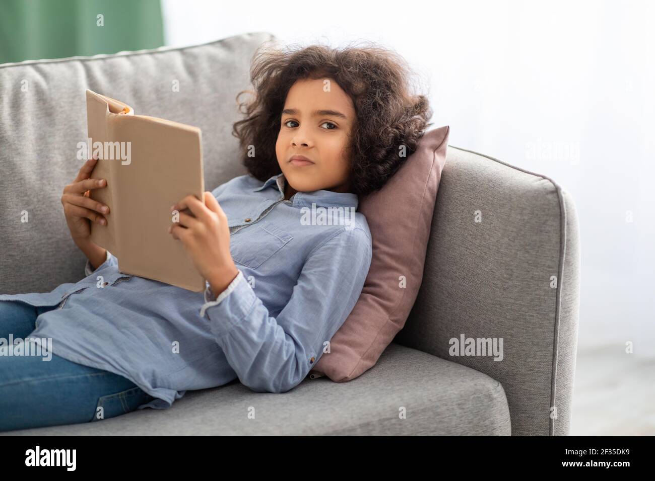Schwarzer Teenager auf der Couch liegend, Buch lesend Stockfoto