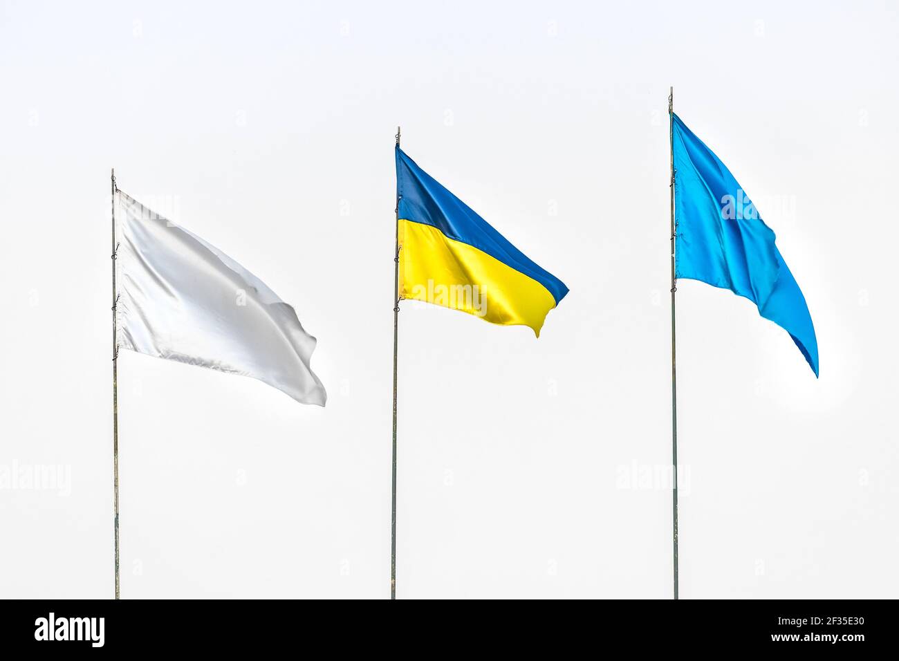 Drei Flaggen: Ukrainische nationale, weiß und blau gegen den grauen Himmel. Stockfoto