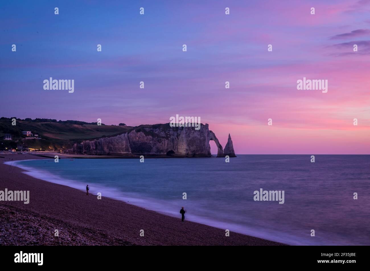 Lange Belichtungszeit von Felsformationen von Porte d'Aval und Aiguille an der Meeresküste gegen den rosa Dämmerungshimmel. Ruhiges Panoramafoto am Abend. Stockfoto