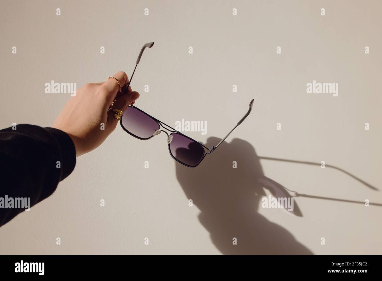 Weibliche Hand hält Sonnenbrille über der weißen Wand. Stockfoto