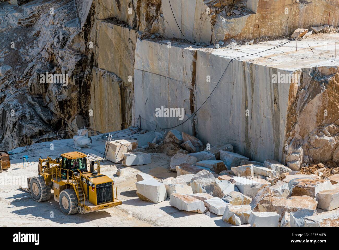 Großer gelber Frontlader, der an riesigen Felsblöcken im Carrara Marmorbruch steht. Bau- und Bergbaurohstoffkonzept. Stockfoto