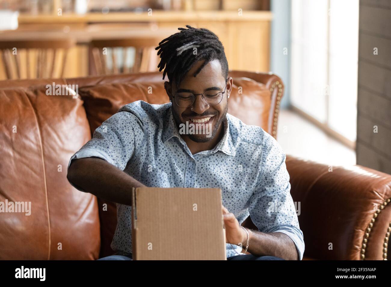 Aufgeregter schwarzer männlicher Webshop-Kunde packt kleinen Karton aus Stockfoto