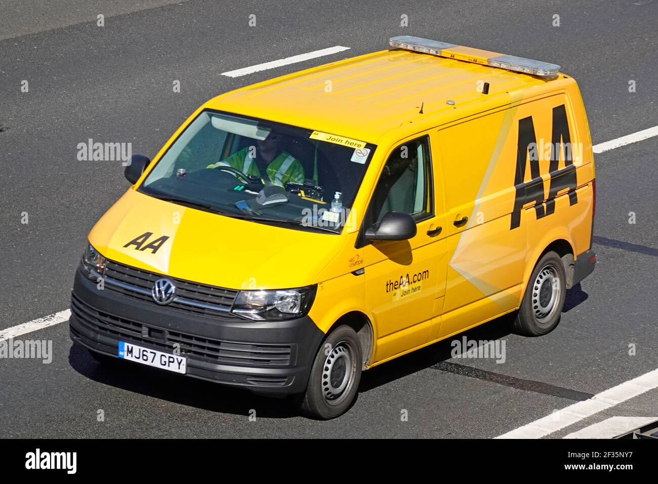 Nahaufnahme Luftaufnahme mit Blick auf den gelben VW Volkswagen Marke AA Pannenwagen & Fahrer in Kabine trägt hoch Sichtweste beim Fahren auf der britischen Autobahn Stockfoto