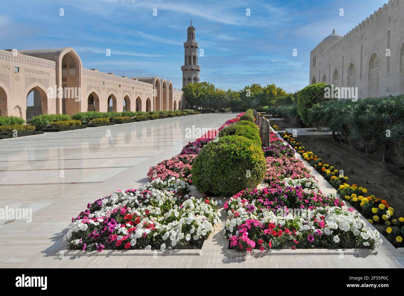 Gepflegter farbenfroher Garten & atemberaubende moderne islamische Architektur Sultan Qaboos Große Moschee poliert weißen Marmor Pflaster & Minarett hinter Muscat Oman Stockfoto