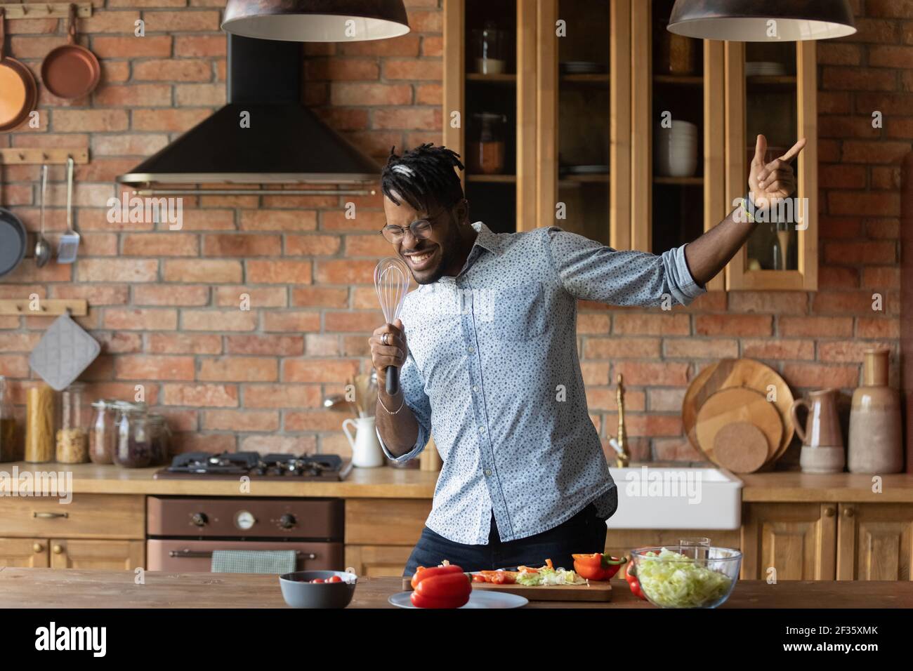 Fröhlicher afro amerikanischer Mann, der in der Küche mit improvisiertem Mikrofon singt Stockfoto