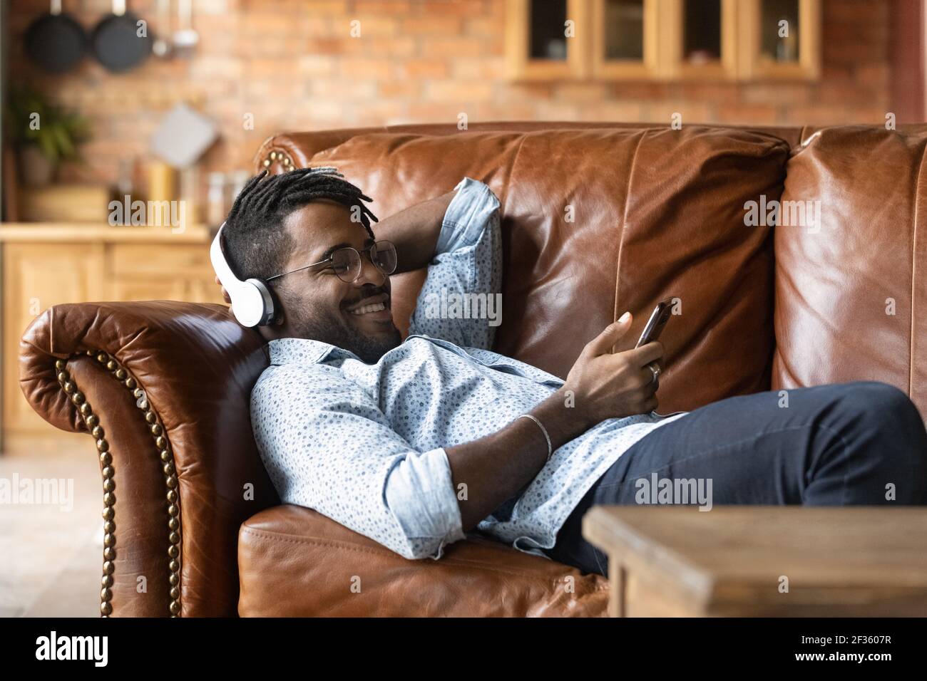 Junger karibischer Mann mit Kopfhörern hört Musik auf dem Handy Stockfoto