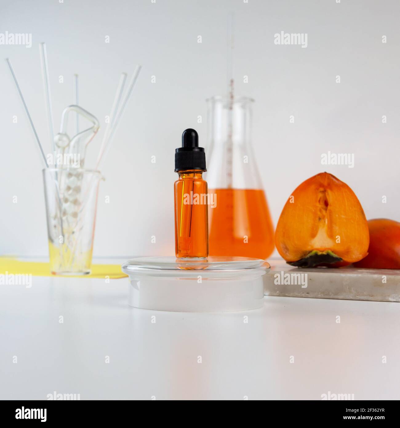 Reife Bio-Persimmonfrucht und Persimmonextrakt in Kosmetikflasche mit Tropf. Abstraktes chemisches oder kosmetisches Labor. Vertikale Aufnahme. Stockfoto