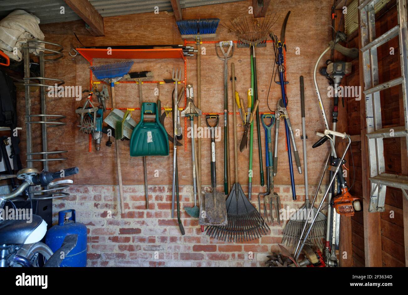 Ein aufgeräumter Schuppen mit an der Wand befestigten Werkzeugen an Clips und Kleiderbügeln. Ein Garten Schuppen Innenraum. Ordentlich angeordnete Gartengeräte. Stockfoto