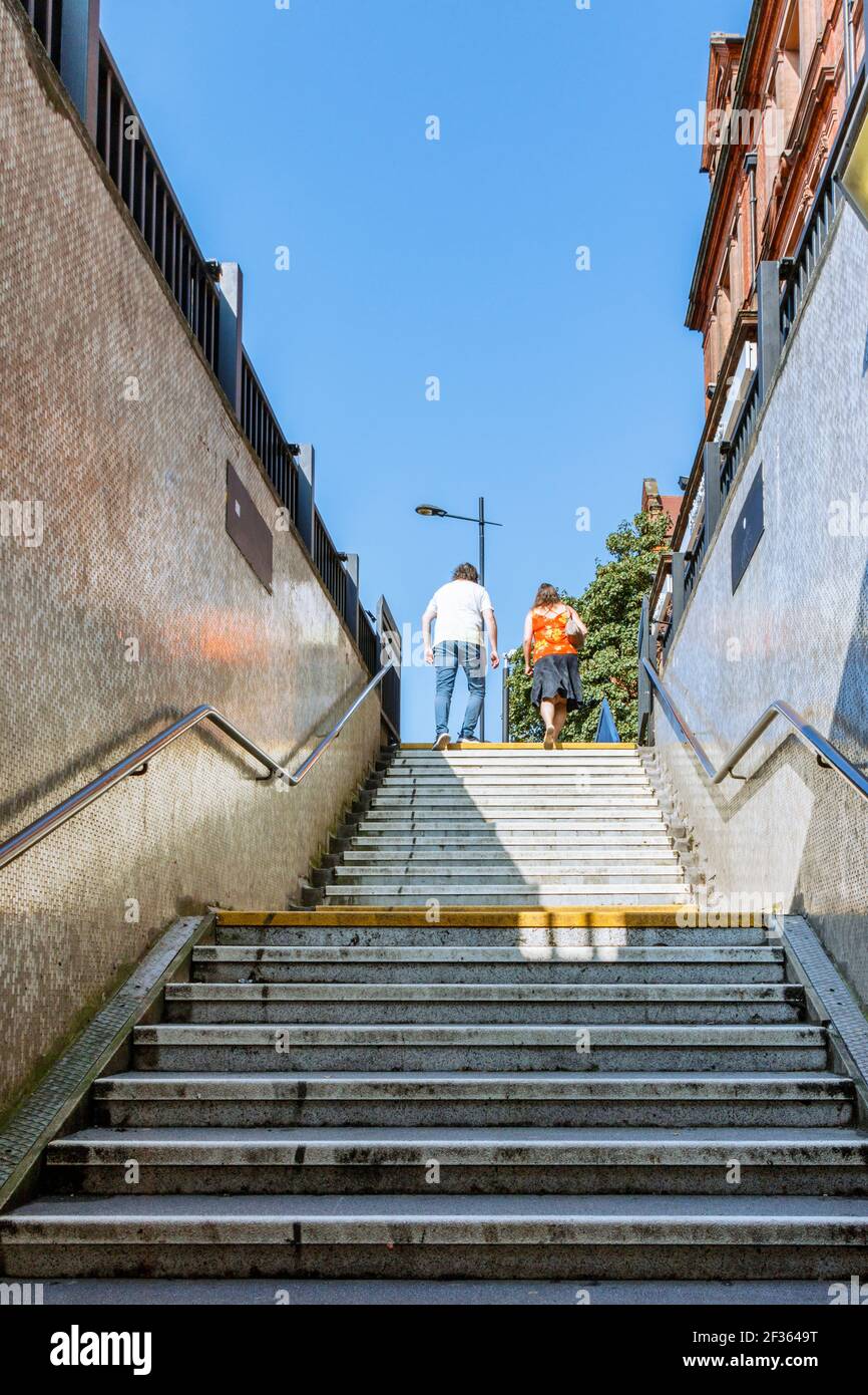 Ein Mann und eine Frau, die aus der U-Bahn-Treppe in London ins Sonnenlicht aufsteigen Stockfoto