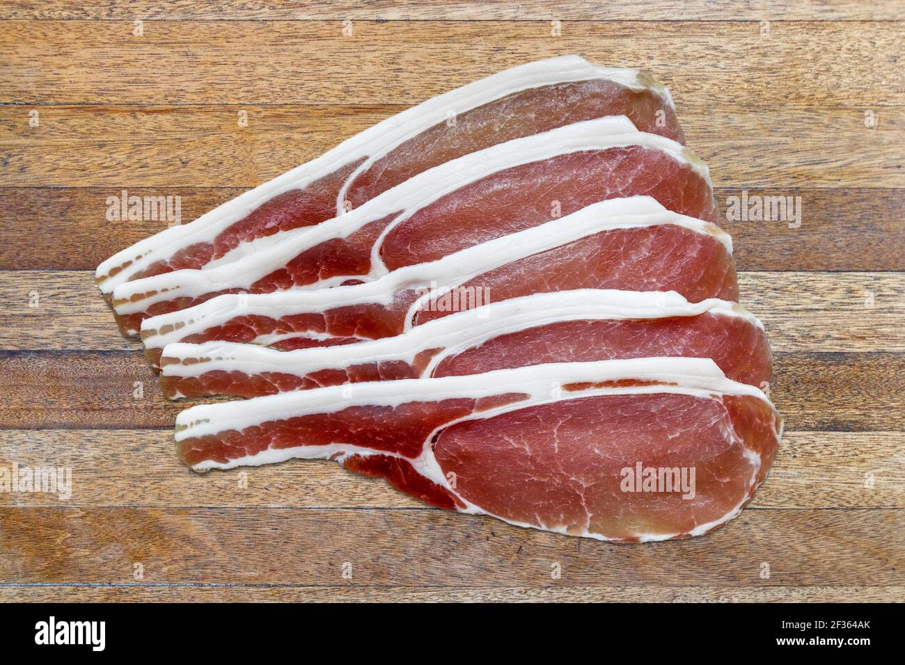 Fünf Rasher von ungegeräuchertem, trocken gehärtetem Rückenspeck auf einem braunen Holztisch mit Lattenrost Stockfoto