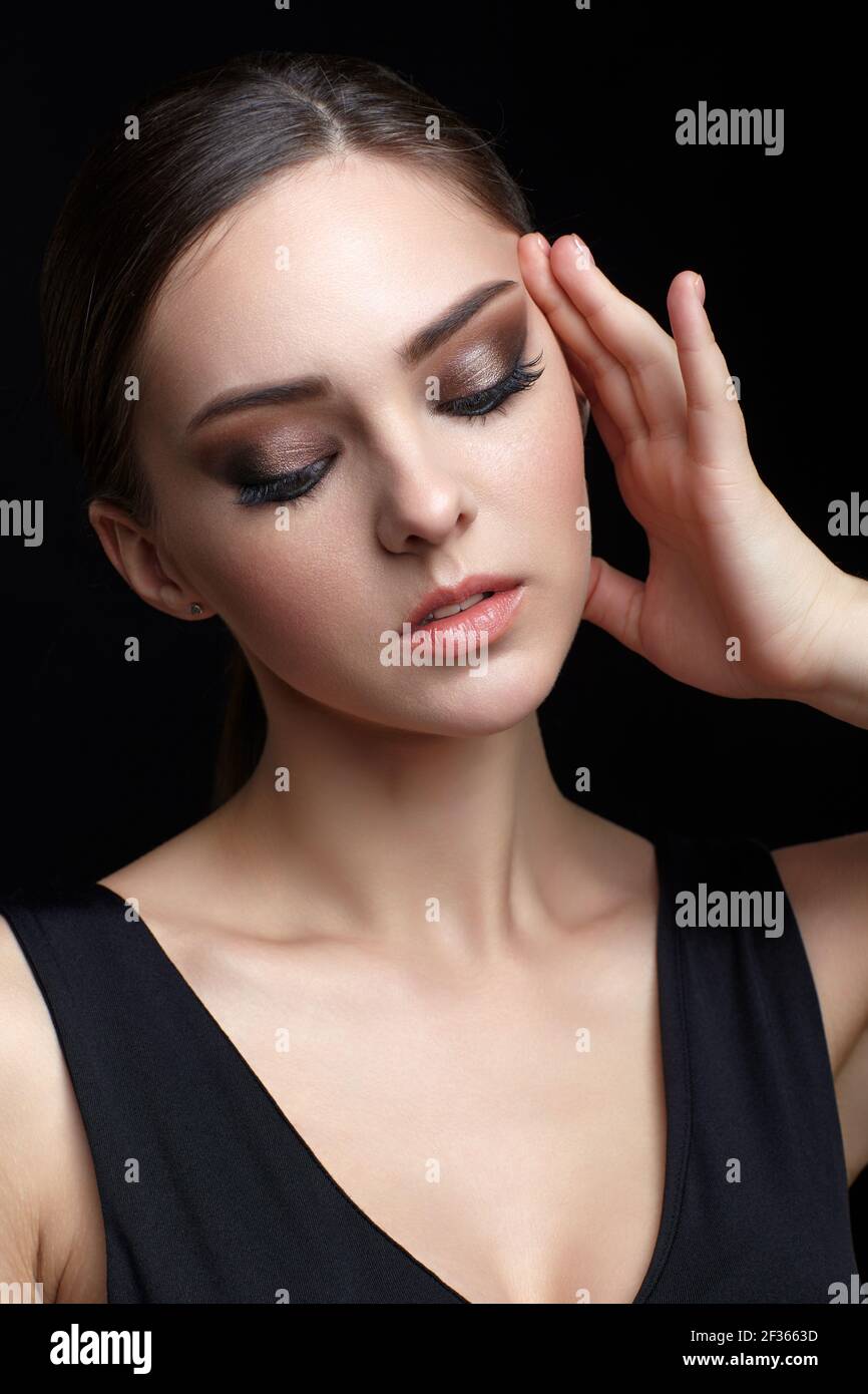 Beauty-Porträt der jungen Frau mit der Hand in der Nähe des Gesichts auf schwarzem Hintergrund. Brunette Mädchen mit Abend weibliche Make-up und schwarz dess berührt Gesicht mit fing Stockfoto