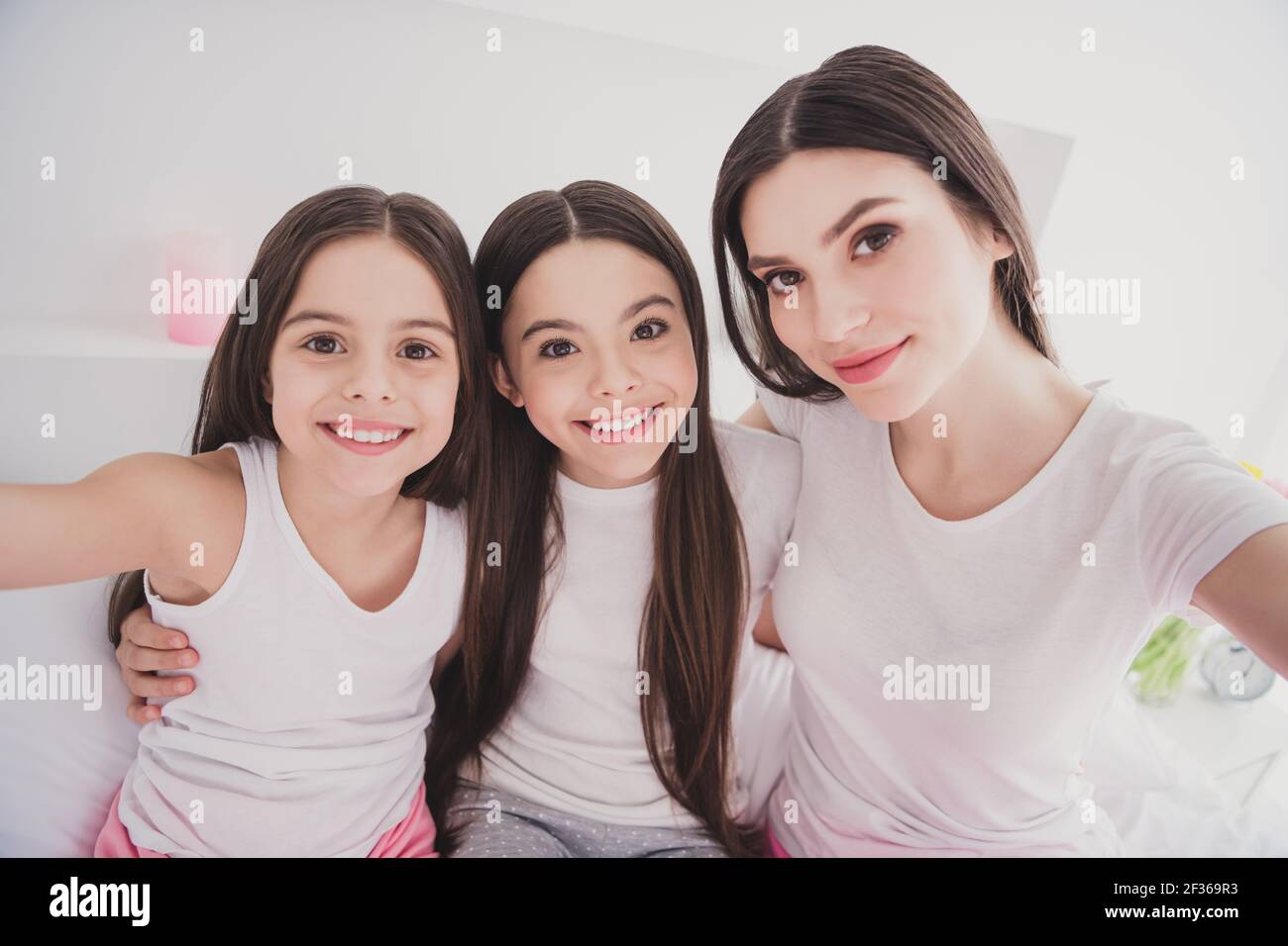 Foto von liebenswert süß drei Geschwister Nachtwäsche sitzend Bett lächelnd Umarmt tacking Selfie drinnen im Zimmer zu Hause Stockfoto