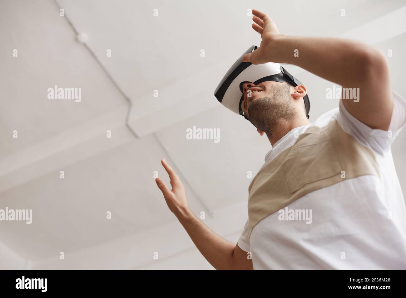 Extreme Low-Angle-Ansicht auf jungen Mann mit VR und Ausgreifen gegen weiße Decke, kopieren Raum Stockfoto