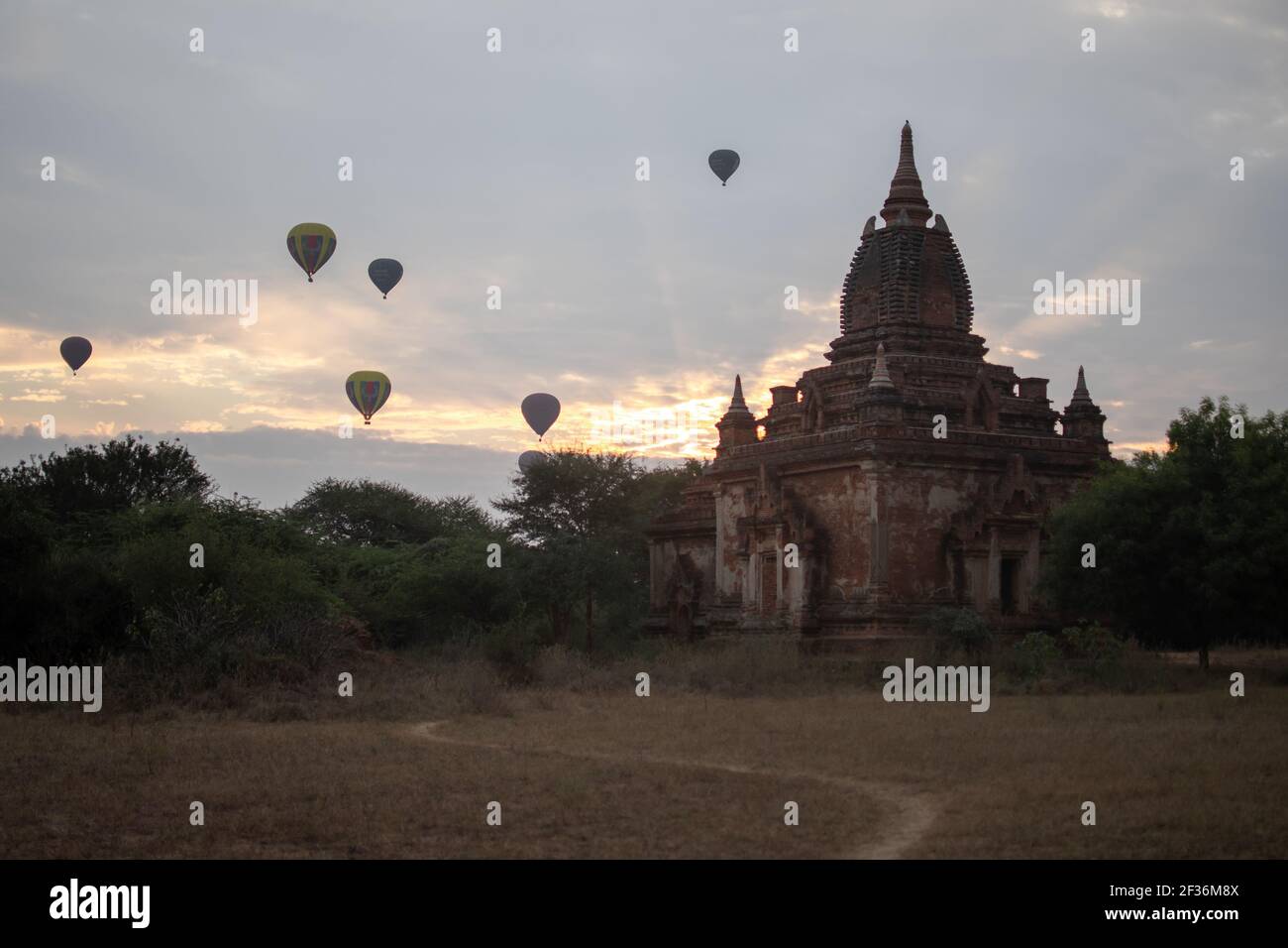 BAGAN, NYAUNG-U, MYANMAR - 2. JANUAR 2020: Ein paar Heißluftballons steigen hinter einem historischen Pagodentempel während des frühen Morgensonnenaufgangs auf Stockfoto