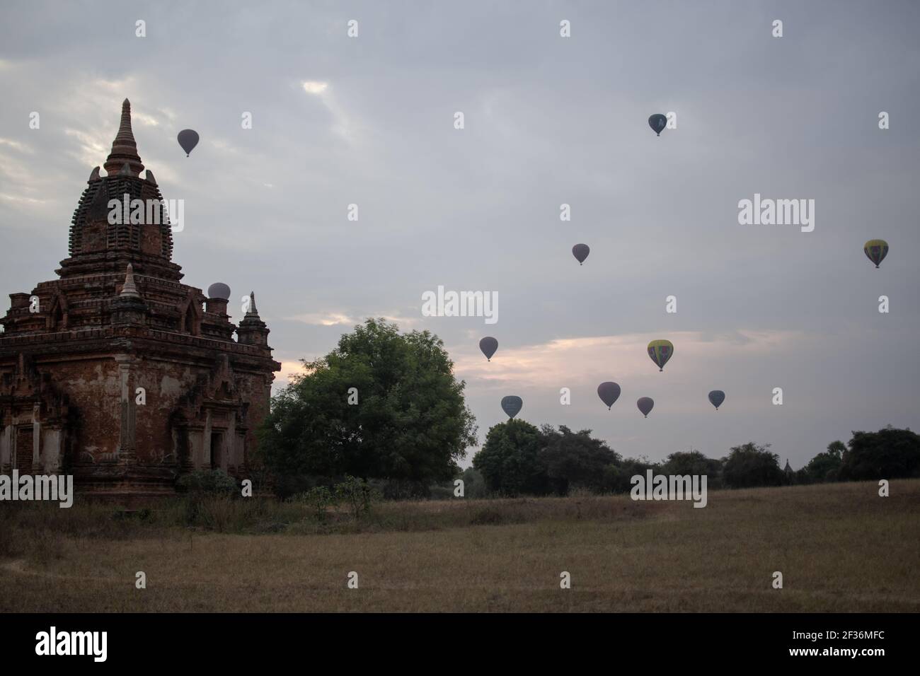 BAGAN, NYAUNG-U, MYANMAR - 2. JANUAR 2020: Ein paar Heißluftballons steigen hinter einem historischen Pagodentempel während des frühen Morgensonnenaufgangs auf Stockfoto