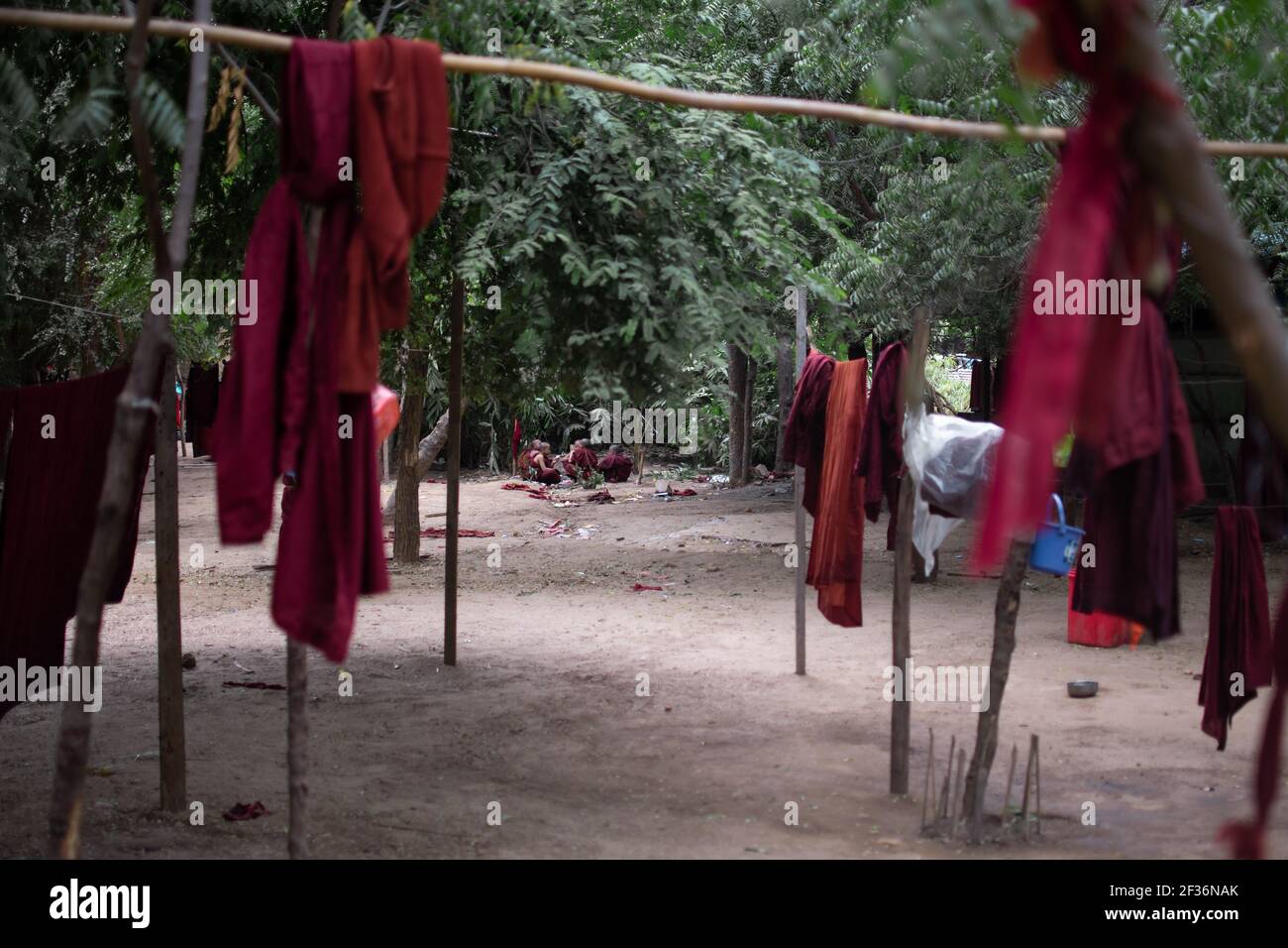BAGAN, NYAUNG-U, MYANMAR - 2. JANUAR 2020: Ein paar junge Mönche sitzen auf dem Boden in einem Wald Clearance hinter einigen buddhistischen roten Roben hängen Stockfoto