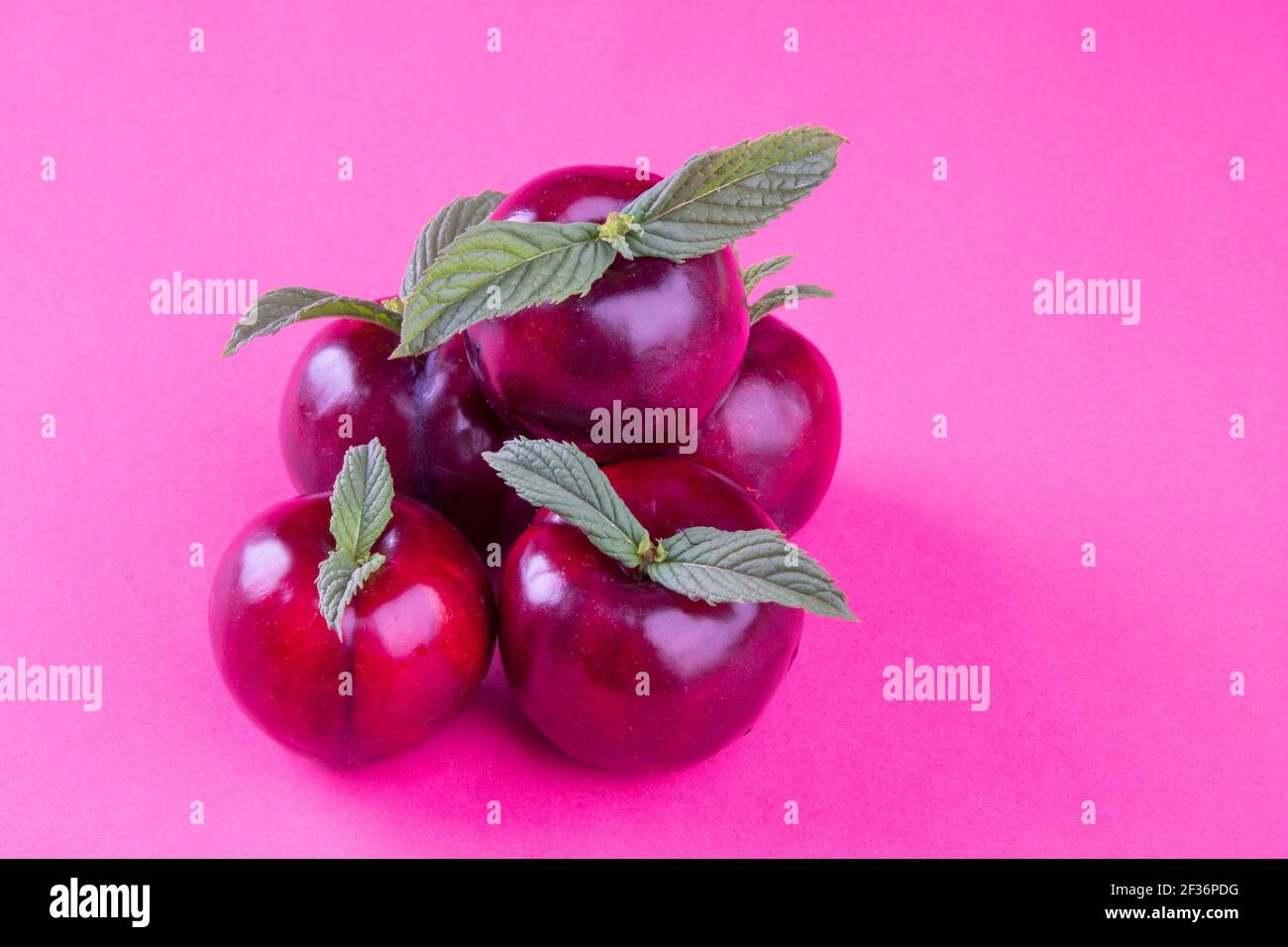 Gesunde Frucht und rosa Farbkonzept: Eine Gruppe von lila roten tropischen Pflaumen mit grünen Blättern. Natürliche Nahrung Hintergrund in fuchsia Stockfoto