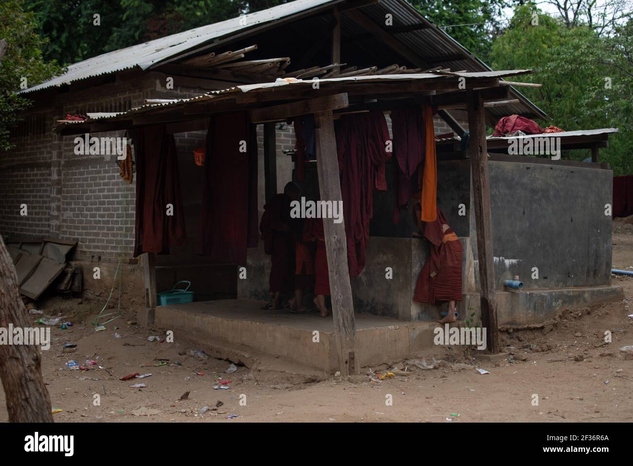 BAGAN, NYAUNG-U, MYANMAR - 2. JANUAR 2020: Ein paar junge Mönche stehen an einem Wasserbrunnen neben einem Haus, wo rote buddhistische Roben hängen trocknet Stockfoto