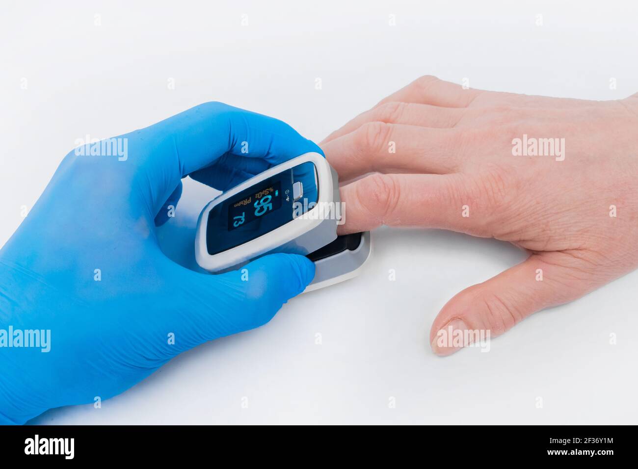 Die Hand des Arztes in einem medizinischen Latexhandschuh hält ein Gerät,  um Sauerstoff im Blut zu messen, Pulsexymeter mit dem Finger einer älteren  Frau auf einem weißen Stockfotografie - Alamy