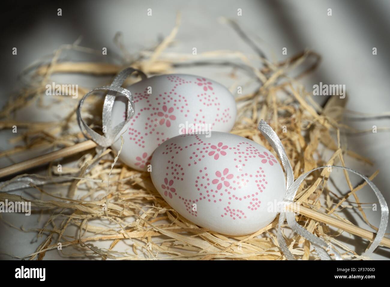 Zwei weiße Eier im Heu, schöner Hintergrund mit Schatten Stockfoto