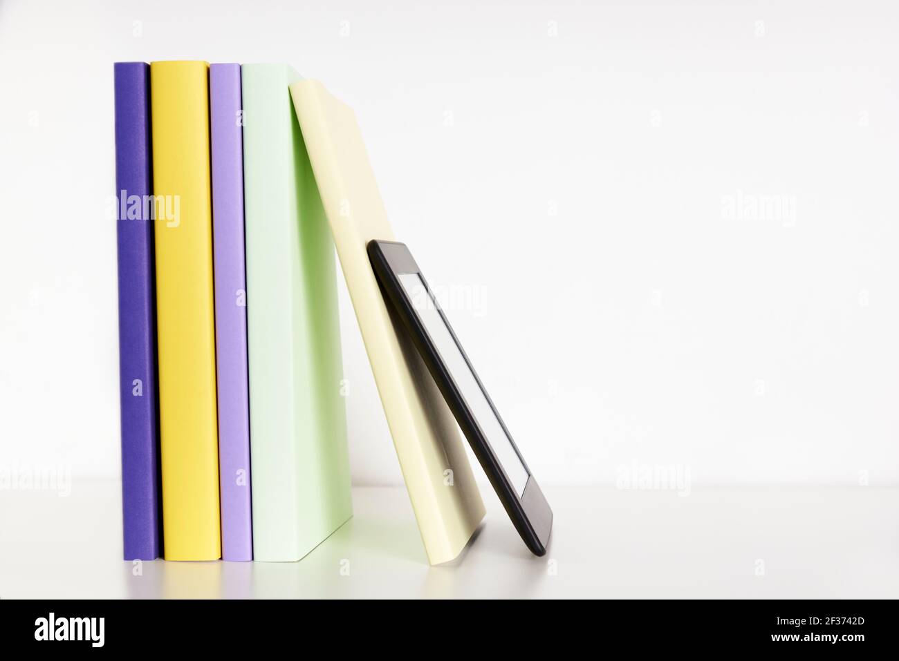 Farbige Bücher mit leerem Rücken und einem elektronischen Leser auf einem weißen Regal mit weißem Hintergrund. Konzepte der Technik, des Lesens und der Bildung. Hell Stockfoto
