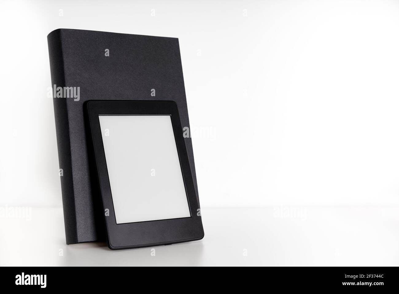 Schwarzes Buch mit leerem Rücken und Frontcover und einem elektronischen Leser auf einem weißen Regal mit weißem Hintergrund. Konzepte der Technologie, Lesen und Educa Stockfoto