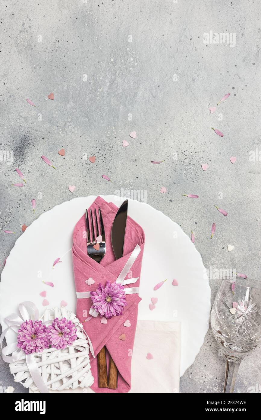 Schöne festliche Tischdekoration mit weißem Teller, Serviette, Blumen und Herzen auf grauem Steinhintergrund. Draufsicht mit Kopierbereich. Stockfoto