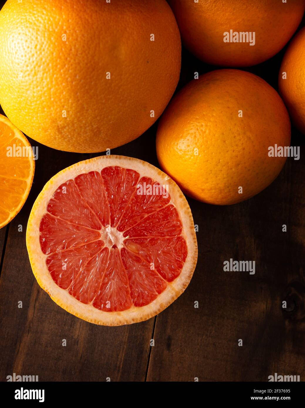 Nahaufnahme von reifen Grapefruitscheiben und mehreren ganzen Orangen Auf braunem rustikalem Holztisch mit Kopierraum Stockfoto